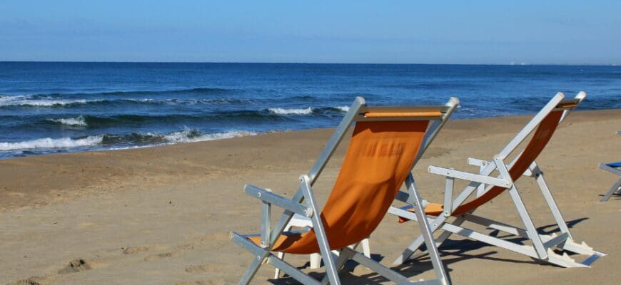 Two foldable beach chairs set out on the sand in front of the water at a beach